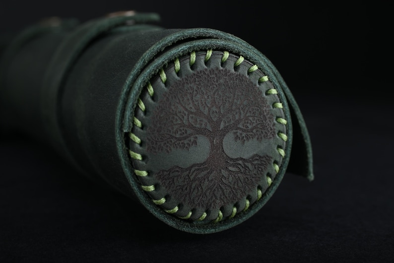 May include: A dark green leather roll with a light green stitched border. The roll has a tree of life design embossed in the center.