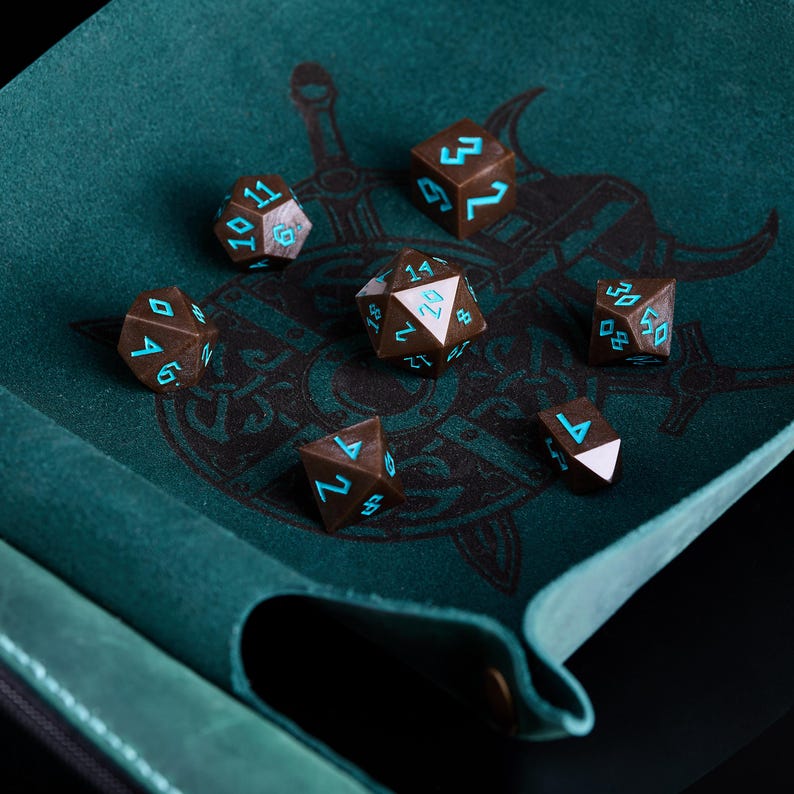 Pu&ograve; includere: Un set di dadi poliedrici marroni con numeri turchese, appoggiati su una superficie di feltro verde acqua. I dadi sono disposti su un tappetino da gioco con un design grafico nero. Per giochi di ruolo.