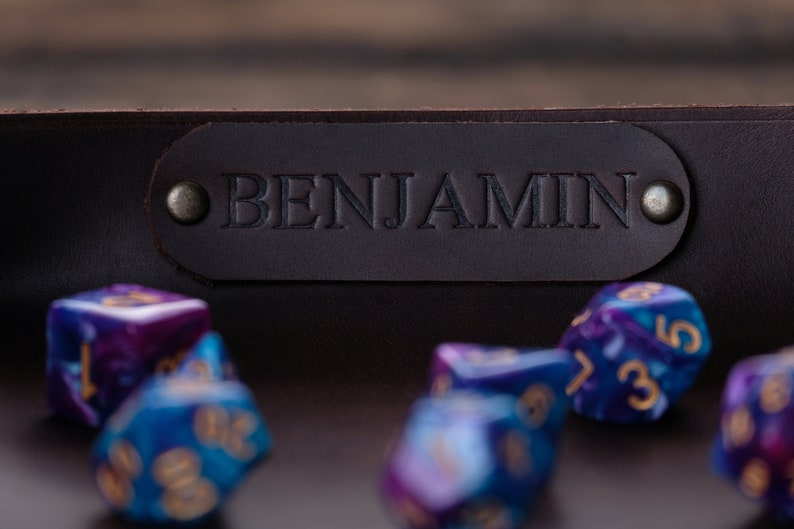 May include: A brown leather dice tray with the name "BENJAMIN" embossed on the front. The tray is filled with colorful dice.