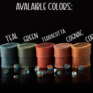 May include: Five cylindrical leather dice cases with stitched edges, labeled with the text AVALAIBLE COLORS: TEAL, GREEN, TERRACOTTA, COGNAC, and COPPER. Each case is accompanied by a small collection of multi-faceted polyhedral dice in various colors.