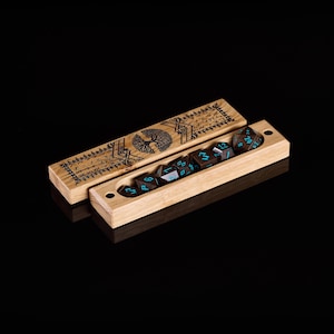 Pu&ograve; includere: Set di dadi in legno con un disegno di albero intagliato sul coperchio. Il set include sette dadi poliedrici con numerazione turchese, riposti in una scatola di legno abbinata. La scatola &egrave; aperta, rivelando i dadi. Lo sfondo &egrave; nero.