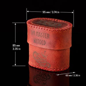 May include: An oval red leather container with stitched edges, featuring the engraved text DM MASTER WITOLD and D&D on the lid. The container measures 3.74 inches in width, 3.35 inches in height, and 2.36 inches in depth, with a dragon graphic.