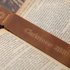Pode incluir: Um marcador de p&aacute;gina de couro castanho com um desenho de floco de neve e o texto "Christmas 2020" em relevo.