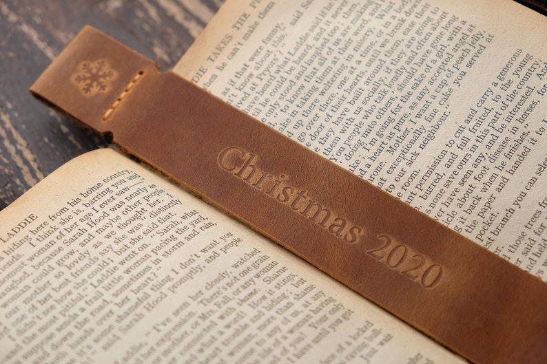 Pode incluir: Um marcador de p&aacute;gina de couro castanho com um desenho de floco de neve e o texto "Christmas 2020" em relevo.