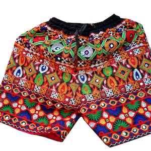 Può includere: Shorts neri con ricami colorati e decorazioni a specchio. I pantaloncini hanno una cintura con coulisse e un motivo geometrico.