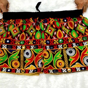 Puede incluir: Shorts negros con bordados coloridos y adornos de espejo. El bordado presenta patrones geométricos en rojo, verde, amarillo y blanco.