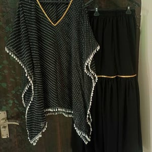 May include: A black and white patterned top with gold trim and white beads, paired with a black skirt with gold trim. The top is a loose-fitting, flowy style.