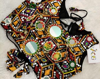 May include: A black, embroidered vest with a geometric pattern in yellow, red, and white. The vest is adorned with small mirrors and sequins, and has black tassels and drawstrings. The overall design is intricate and colorful.