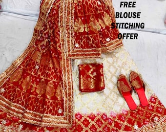 May include: A white and red lehenga with gold embroidery and a red dupatta. The lehenga has a white base with a red border and gold embroidery. The dupatta is red with gold embroidery. The set includes a red blouse with gold embroidery. The text "FREE BLOUSE STITCHING OFFER" is visible in the image.