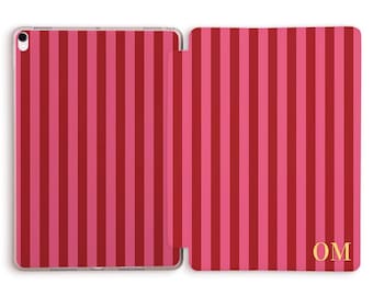 May include: An open iPad case with a vertical striped pattern in shades of pink and red. The case is personalized with the gold initials "OM" on the right side.