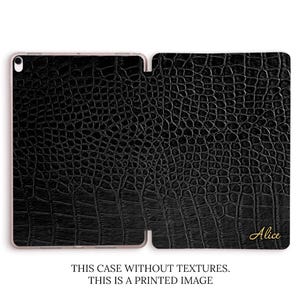 Pode incluir: Capa de tablet preta em couro sintético com textura de pele de crocodilo. A capa está aberta, revelando o interior. O nome "Alice" está impresso em dourado no canto inferior direito. O texto "THIS CASE WITHOUT TEXTURES. THIS IS A PRINTED IMAGE" está impresso na parte inferior.