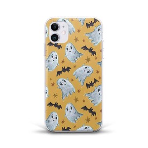 May include: A clear phone case featuring a repeating pattern of cartoon ghosts, bats, and stars on a mustard yellow background. The ghosts are white with smiling faces, and the bats are black. The case is designed for a smartphone.