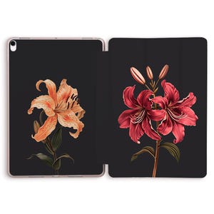 May include: A tablet case featuring a floral design. The case is black with two detailed illustrations of lilies. One lily is orange with brown spots, and the other is a deep red. Green leaves and stems accompany the flowers.