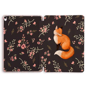 May include: Tablet case with a watercolour fox illustration on a dark background, adorned with pink flowers and white branches. The case is open, showing the design on both sides. A charming woodland theme.
