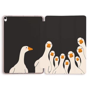Può includere: Una custodia per tablet con un design a cartoni animati di oche. La custodia è nera con un bordo rosa. Le oche bianche hanno becchi e zampe arancioni, disposte in un motivo giocoso, creando un design divertente e accattivante.