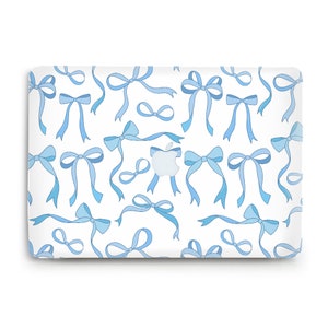 May include: A white laptop skin with a repeating pattern of blue bows. The bows are drawn in a simple, cartoon style.