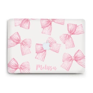 May include: A white laptop case featuring a pattern of pink gingham bows. An Apple logo is centered on the case, with the name "Melissa" in a cursive font below the logo. The bows are in a watercolor style.