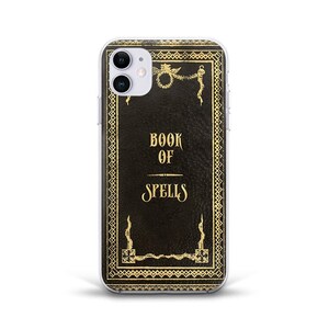 May include: A clear phone case with a black and gold design. The design features a book with the words "Book of Spells" on the cover.