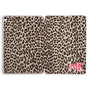 Può includere: Custodia per tablet aperta con un motivo leopardato marrone e beige. La custodia è aperta, rivelando l'interno e l'esterno. Le iniziali "MK" sono stampate in rosa nell'angolo in basso a destra della custodia.