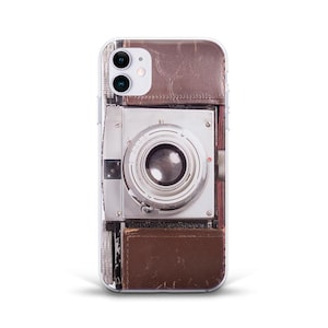 May include: A clear phone case with a vintage camera design. The camera is brown and silver with a large lens. The case is designed to fit an iPhone.