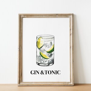 May include: Framed art print featuring a watercolor illustration of a gin and tonic cocktail. The drink is in a tall glass with ice and lime wedges. The words "GIN & TONIC" are printed below the image in a black, sans-serif font.