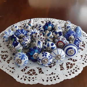 May include: A collection of blue and white ceramic drawer knobs with floral patterns. The knobs are arranged on a white doily.