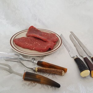 Könnte beinhalten: Zwei rohe Rinderfilets auf einem braunen und weißen Teller mit drei Steakmessern und zwei Steakgabeln mit braunen Griffen.