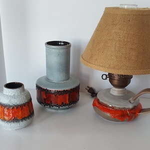 May include: Three ceramic vases with a blue glaze and orange and brown accents. The vases are in different sizes and shapes. The largest vase is a tall cylinder with a wide base. The medium vase is a round vase with a wide mouth. The smallest vase is a round vase with a narrow mouth. The vases are all decorated with a band of orange and brown glaze around the middle.
