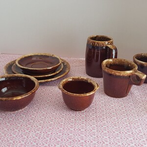 May include: A set of brown and tan glazed pottery includes a large mug, two small mugs, a bowl, and a saucer with a smaller saucer inside.