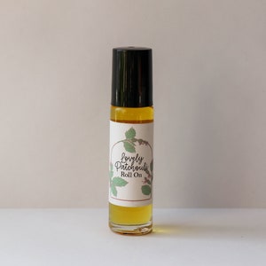 May include: A clear glass roll-on bottle with a black cap, filled with a yellow liquid. The label reads "Lovely Patchouli Roll On" with a botanical design. The bottle is approximately 4 inches tall.