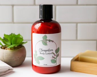May include: Red plastic bottle of Cleopatra Body Lotion with a white label featuring a green plant illustration. The label also includes the text "Cleopatra Body Lotion" and "8 oz."