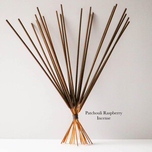 May include: A bundle of incense sticks, tied together with a dark brown cord. The incense sticks are a light brown color, and the text "Patchouli Raspberry Incense" is visible.