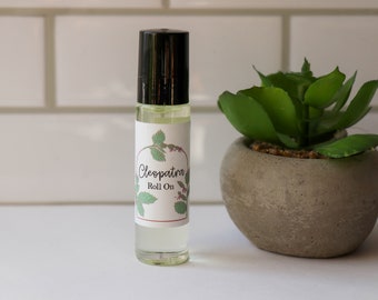 May include: A clear glass roll-on bottle with a black cap and a white label that says "Cleopatra Roll On". The label has a green leaf design.