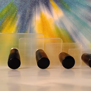 May include: Four clear, rectangular grout floats with black handles. The floats are arranged in a row, decreasing in size from left to right. The background is a colorful abstract design with yellow, blue, and green hues.