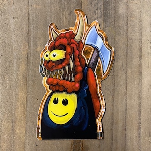 May include: A red and yellow cartoon monster with a big smile and a blue shirt with a yellow smiley face. The monster is holding a blue axe with a brown handle. The background is a gold and brown pattern.
