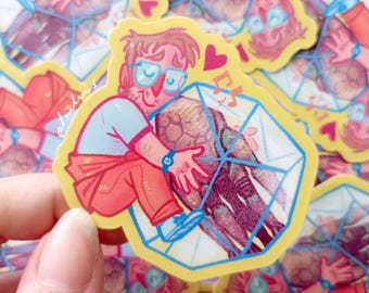 Op de afbeelding: Een sticker met een cartoon illustratie van een persoon die een geometrische vorm omarmt. De persoon draagt een bril, een blauw horloge en een oranje broek. De sticker heeft een gele rand en de tekst "@lirandraws".
