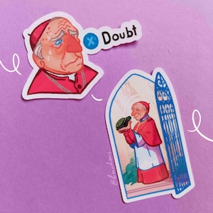 May include: Two stickers on a purple background. One sticker features a cartoon of a man in a red robe and hat with the word "Doubt". The other sticker shows a man in a red robe and hat holding a green hat.