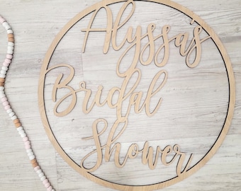 May include: A wooden circle sign with the text "Alyssa's Bridal Shower" in cursive script.