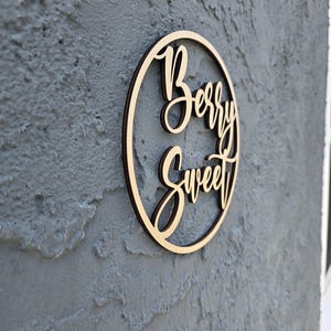 May include: A wooden circle sign with the words "Berry Sweet" written in cursive script.