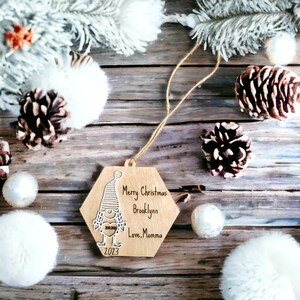 May include: A hexagonal wooden Christmas bauble featuring a white gnome design. The bauble is personalised with the text "Merry Christmas Brooklyn Love, Momma 2023".