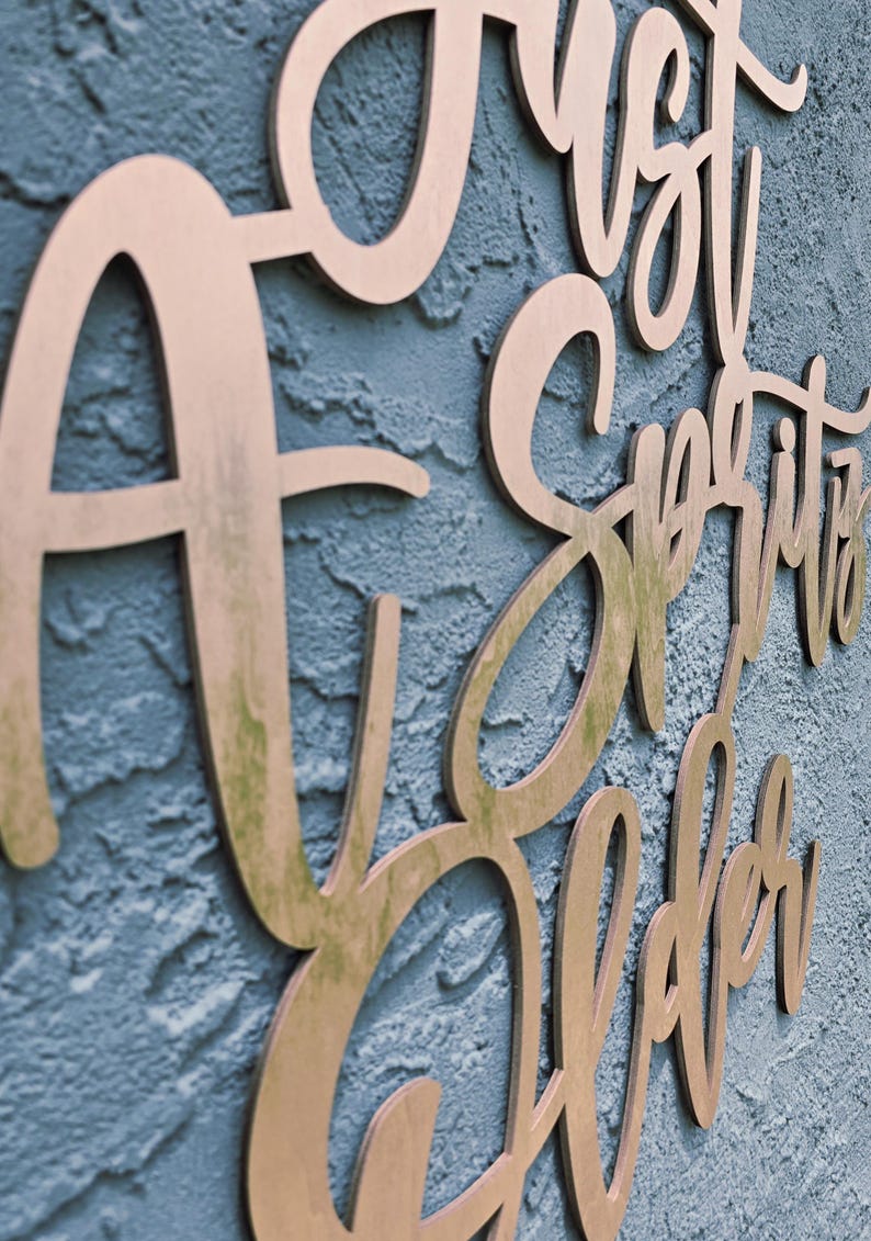 Puede incluir: Letrero de madera con la frase "A Just Spirits Sober" en fuente cursiva. El letrero est&aacute; hecho de madera marr&oacute;n claro y montado en una pared azul texturizada. Las letras est&aacute;n recortadas y tienen una ligera sombra.