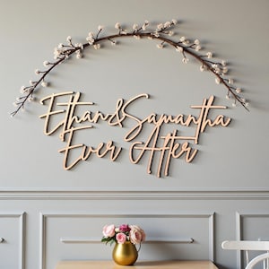 Puede incluir: Arte mural de madera con los nombres "Ethan & Samantha" y la frase "Ever After" en cursiva. Una rama floral arqueada sobre los nombres. La pared es gris y debajo hay un jarr&oacute;n dorado con rosas rosas.