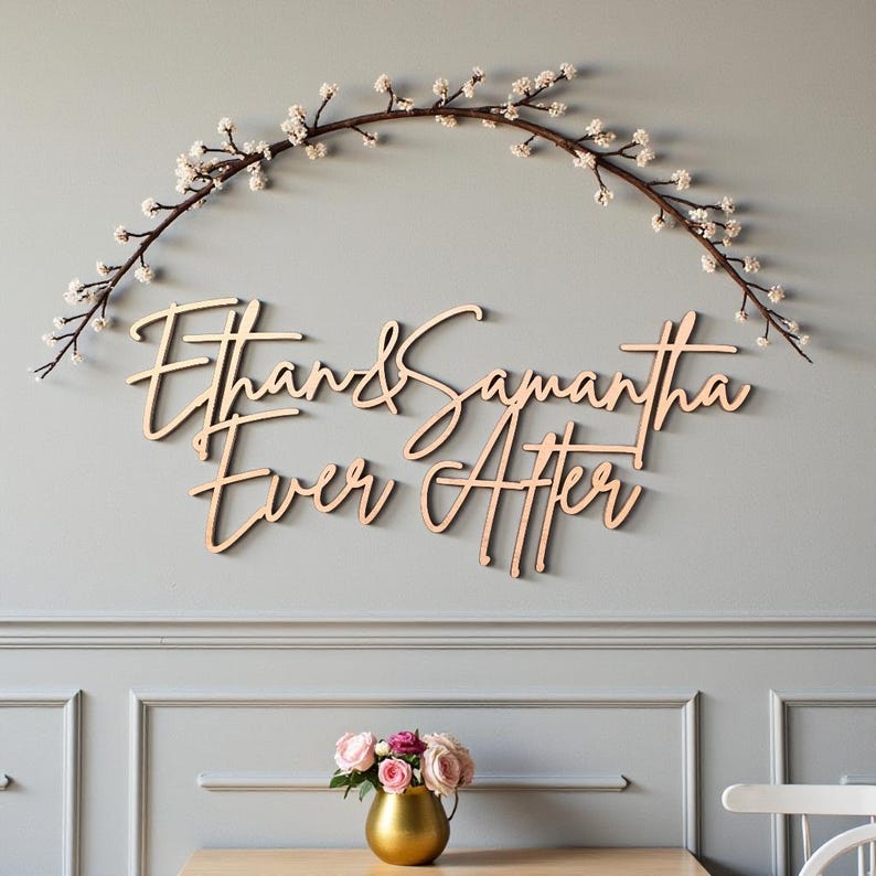 Puede incluir: Arte mural de madera con los nombres "Ethan & Samantha" y la frase "Ever After" en cursiva. Una rama floral arqueada sobre los nombres. La pared es gris y debajo hay un jarr&oacute;n dorado con rosas rosas.