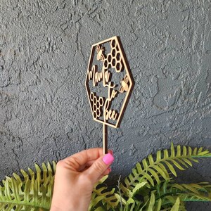 May include: Wooden cake topper shaped like a hexagon with the text "Mama to bee" and three small bees. The hexagon is decorated with honeycomb patterns.