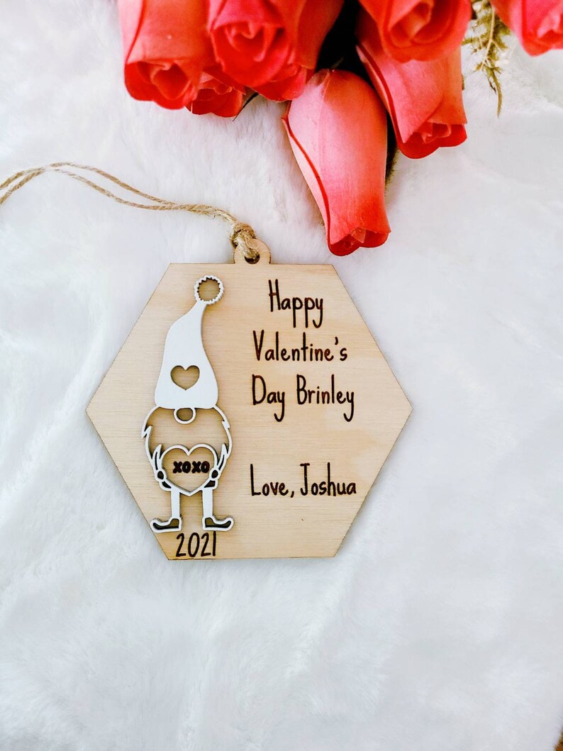 May include: Wooden ornament shaped like a gnome holding a heart with the text "XOXO". The ornament is decorated with the text "Happy Valentine's Day Brinley Love, Joshua 2021".
