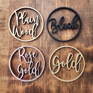 May include: Four wooden circles with different finishes: plain wood, black, rose gold, and gold. Each circle has a word cut out in the center.