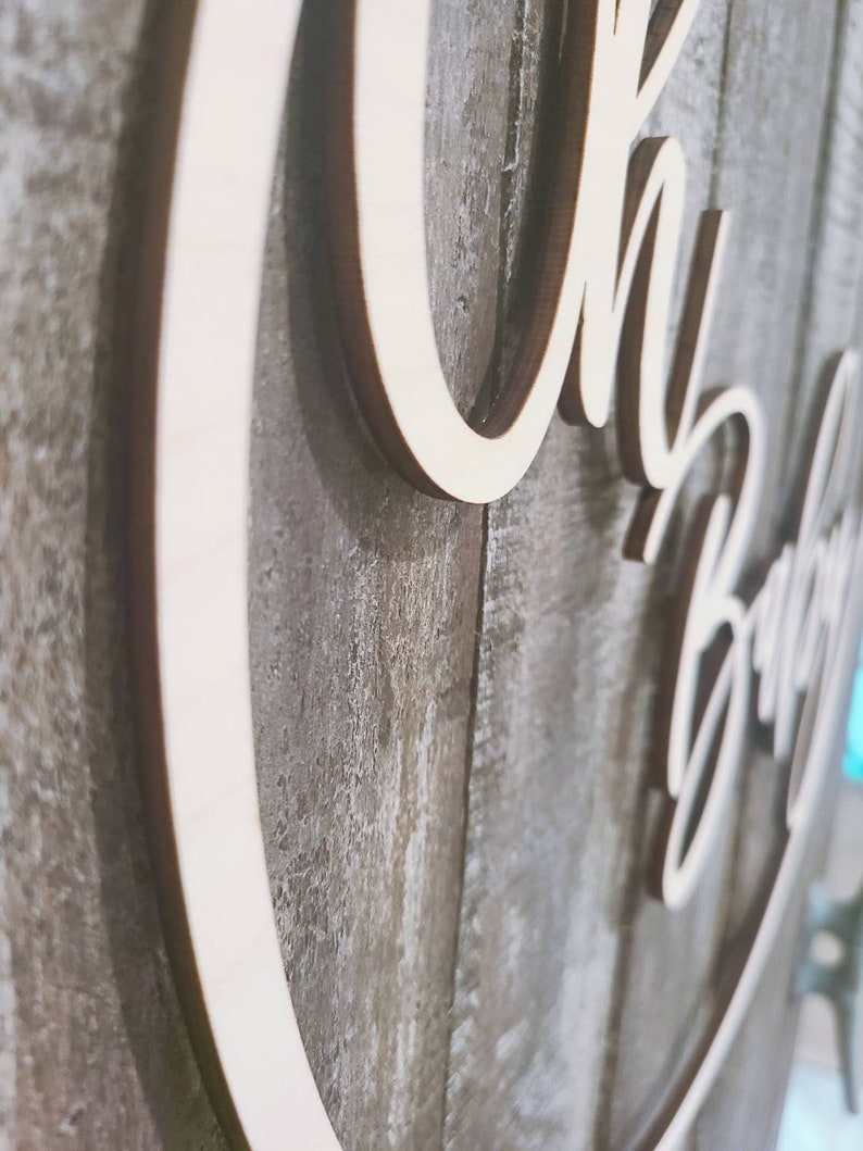 May include: Wooden sign with the words "Oh Baby" in a cursive font. The sign is attached to a rustic wooden background.