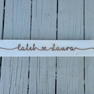 May include: White wooden sign with the names "Caleb" and "Laura" written in cursive with a heart symbol between them.