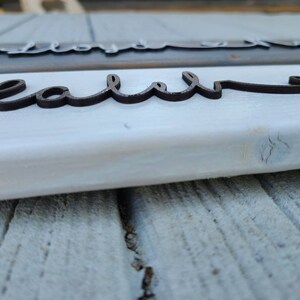 May include: Close-up of a white wooden sign with the word "real" written in black cursive lettering.