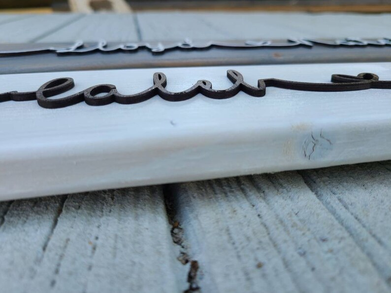 May include: Close-up of a white wooden sign with the word "real" written in black cursive lettering.